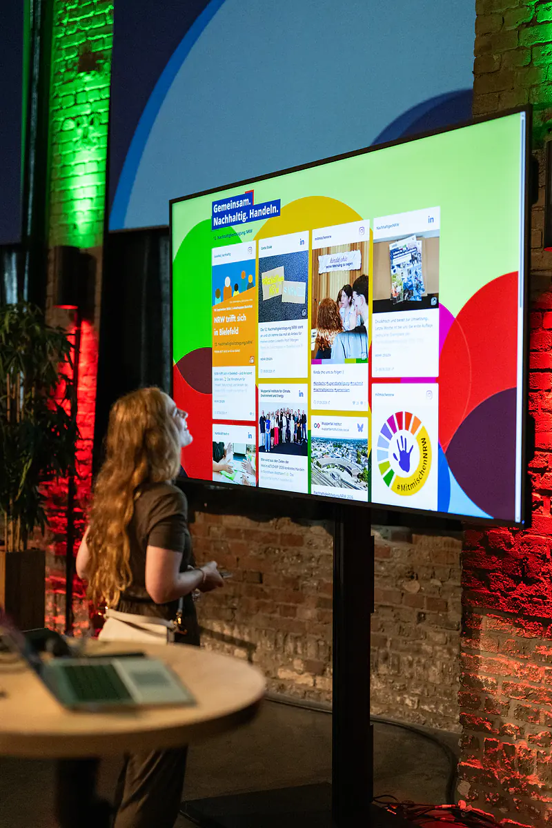 Eine Besucherin betrachtet die digitale Social Wall der Tagung auf einem großen Bildschirm