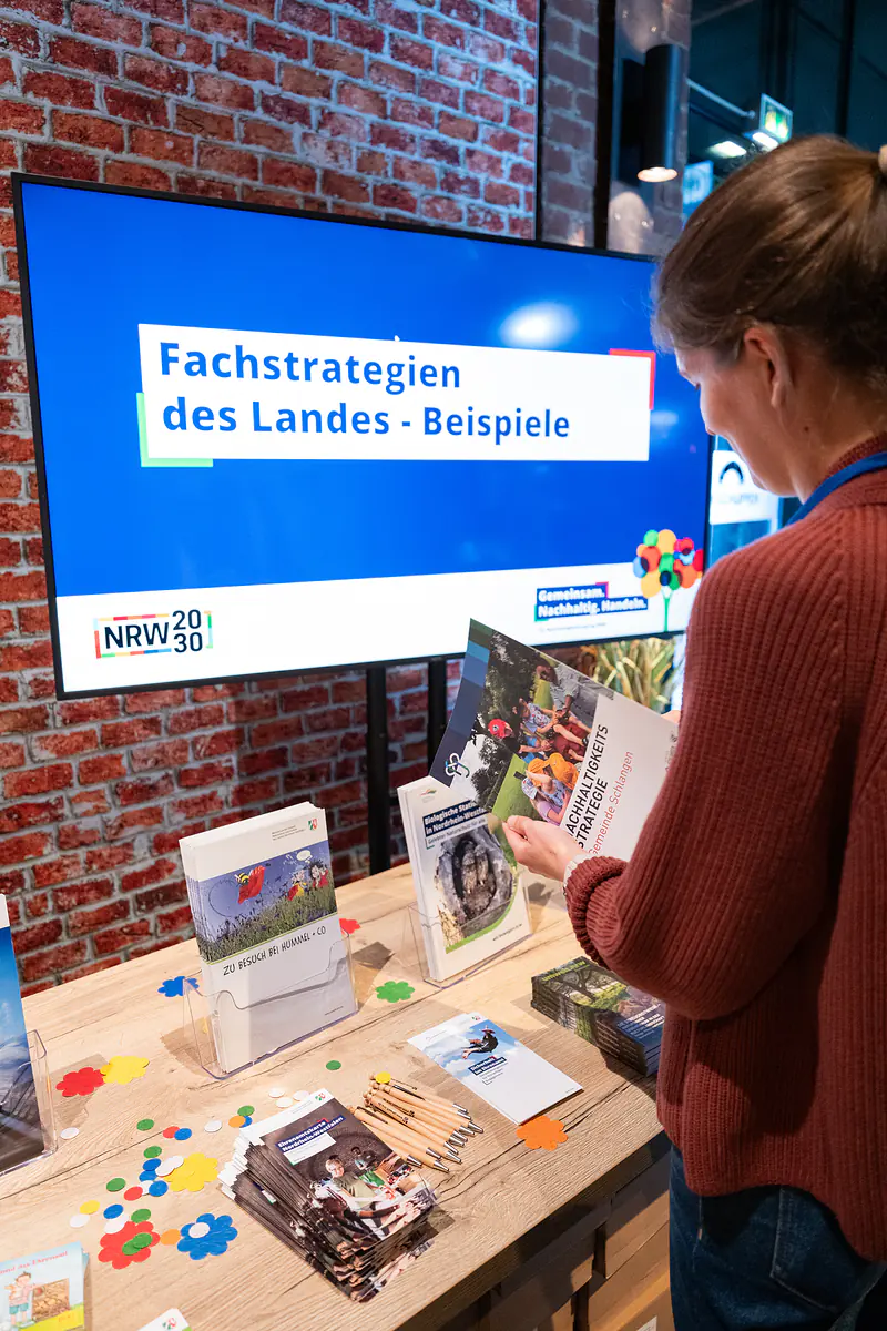 Eine Besucherin blättert am Infostand „Fachstrategien des Landes – Beispiele“ in einer Broschüre