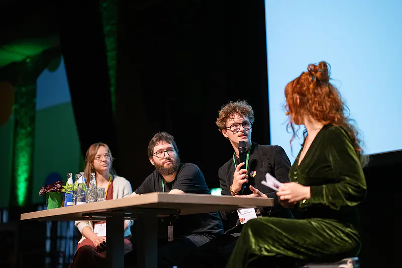 Talkrunde auf der Bühne mit drei jungen Gästen und der Moderatorin, seitlich aufgenommen