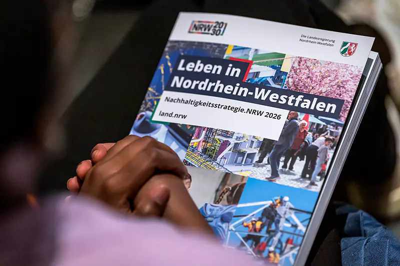 Gefaltete Hände auf der Broschüre „Leben in Nordrhein-Westfalen – Nachhaltigkeitsstrategie.NRW 2026“ im Publikum
