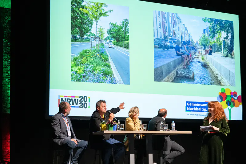 Podium „Ökosystem Kommune“: vier Gäste und die Moderatorin auf der Bühne vor Fotos begrünter Straßen