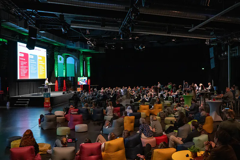 Der Saal während der Keynote: Publikum auf bunten Sitzsäcken vor der Bühne mit Präsentation