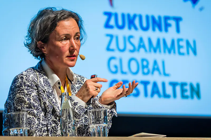 Die Keynote-Rednerin gestikuliert vor dem Schriftzug „Zukunft zusammen global gestalten“
