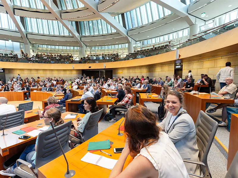 Dieses Foto zeigt Menschen aller Altersklassen, sitzen in einem Saal bei einer vergangenen Nachhaltigkeitstagung.NRW.